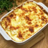 Ein goldbraun gebackenes Kartoffelgratin in einer weißen Auflaufform auf einem Holzuntergrund.