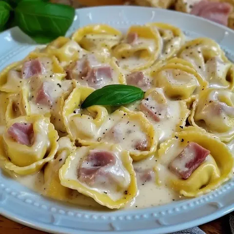 Eine Schüssel mit Tortellini in cremiger Sauce, garniert mit einem Blatt frischem Basilikum.