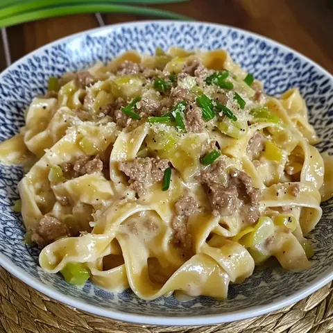 Ein Teller mit Bandnudeln in einer cremigen Sauce, garniert mit Hackfleisch, Lauch, Schnittlauch und Parmesan.