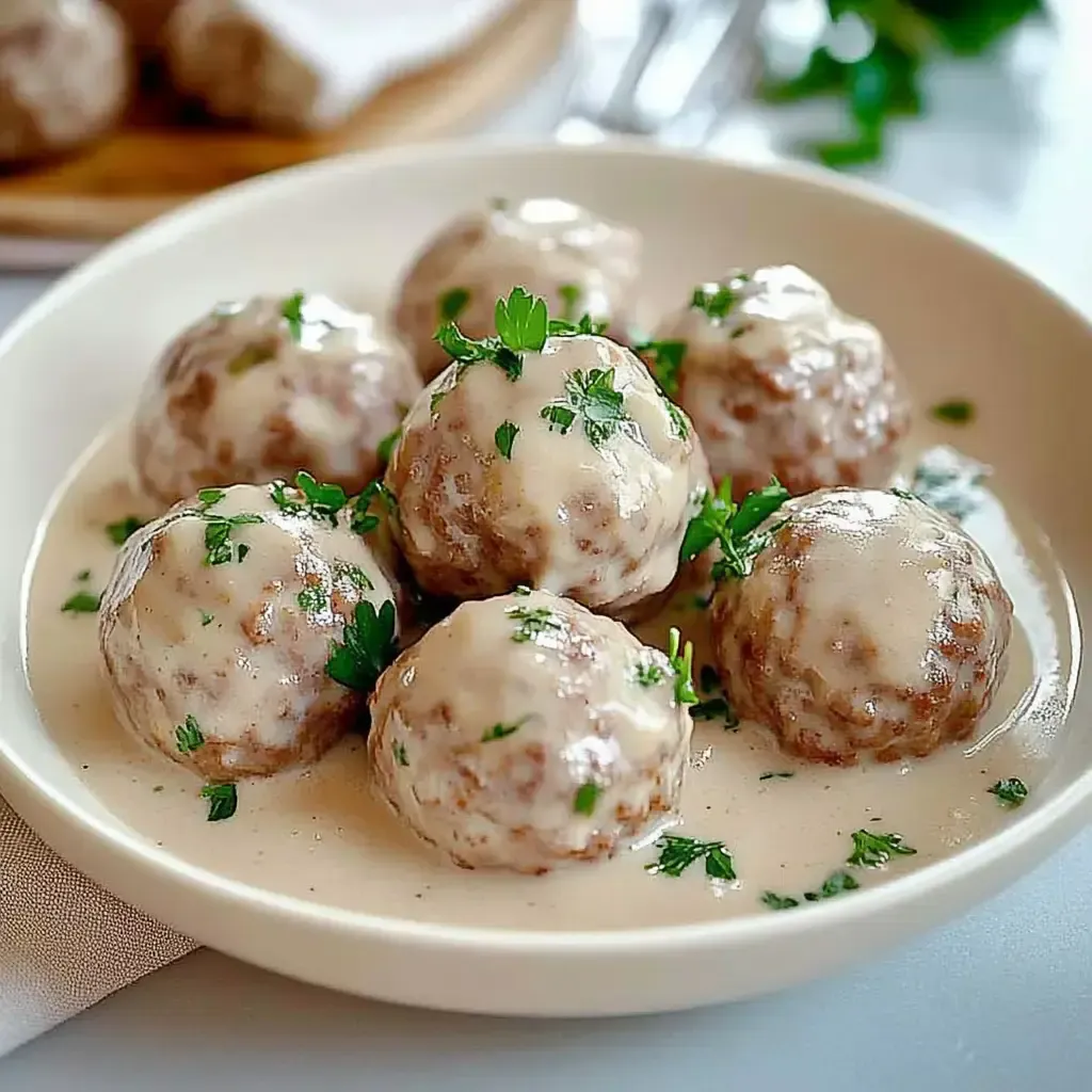 Eine Schüssel mit sieben Fleischbällchen in einer cremigen Sauce, garniert mit frischer Petersilie.