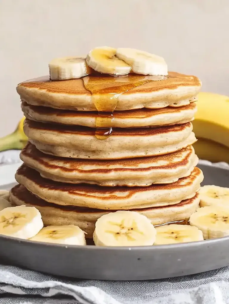 Ein Stapel Pfannkuchen mit Bananenscheiben und Honig auf einem Teller.