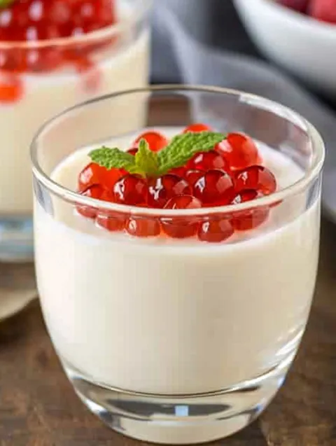 A glass of cream cheese panna cotta with red berries on top.