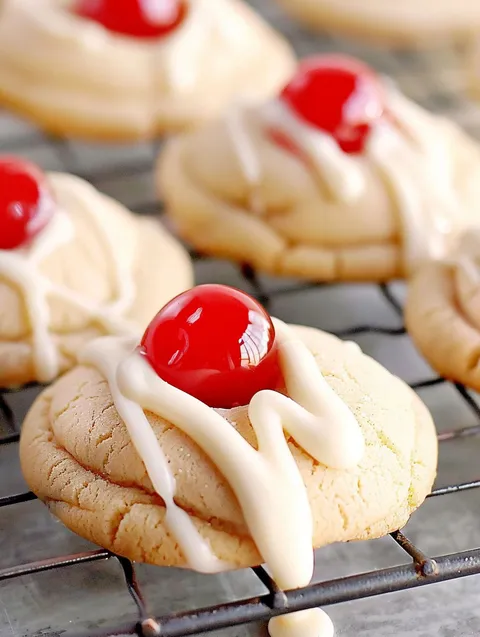 A batch of cookies with cherries on top.