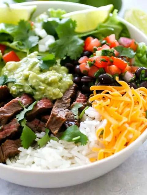 A bowl of food with rice, beans, tomatoes, lettuce, and cheese.