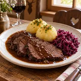 Teller mit Sauerbraten, Kartoffelklößen, brauner Soße und Rotkohl